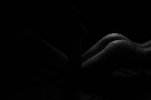 Black and White Beautiful woman body. Fashion art studio portrait of elegant naked lady with shadow on her. Female stomach isolated on black background. Erotic pose low key shoot. - Foto, imagen