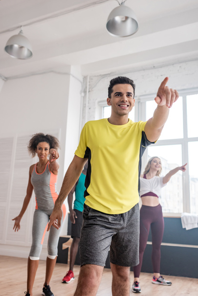 Enfoque selectivo de entrenadores y bailarines multiétnicos apuntando con el dedo mientras bailan zumba en estudio
 - Foto, imagen