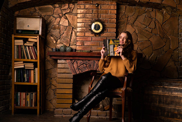привлекательная молодая женщина, сидящая в кресле у камина в студии   - Фото, изображение