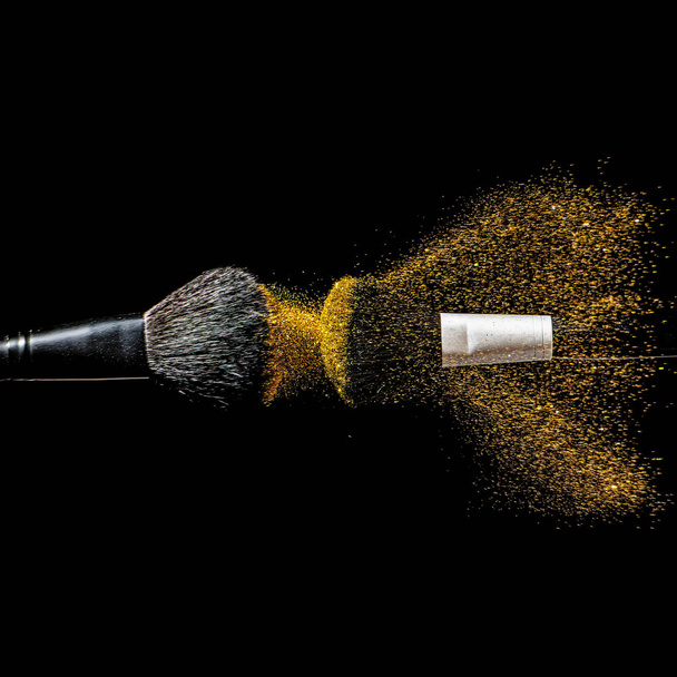 Make-up brush with gold powder explosion on black background. - Photo, Image