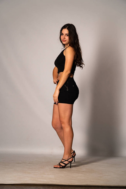 Beautiful woman with dark hair in black clothes posing on light studio background  - Foto, imagen