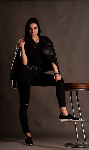 молодая брюнетка в стильной одежде позирует в темной студии   - Фото, изображение
