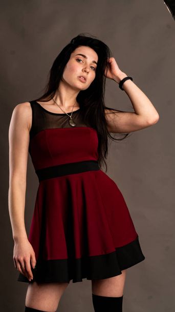 Koyu renk saçlı, kırmızı elbiseli, karanlık stüdyoda poz veren genç ve seksi bir kadın.. - Fotoğraf, Görsel