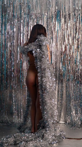 beautiful sexy nude woman in shiny christmas tinsel posing in studio, holiday concept     - Foto, afbeelding