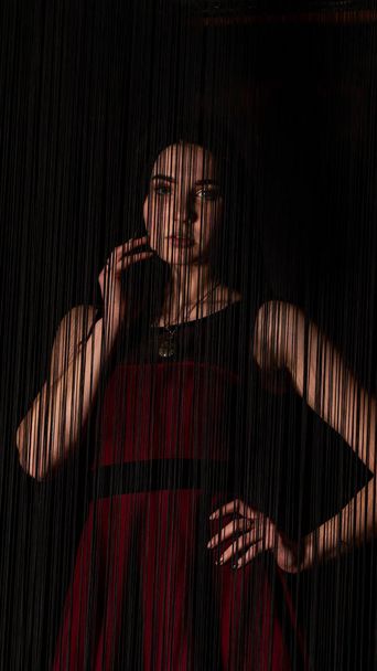 Muito jovem modelo sexy feminino com cabelos escuros em vestido vermelho posando em estúdio escuro. - Foto, Imagem