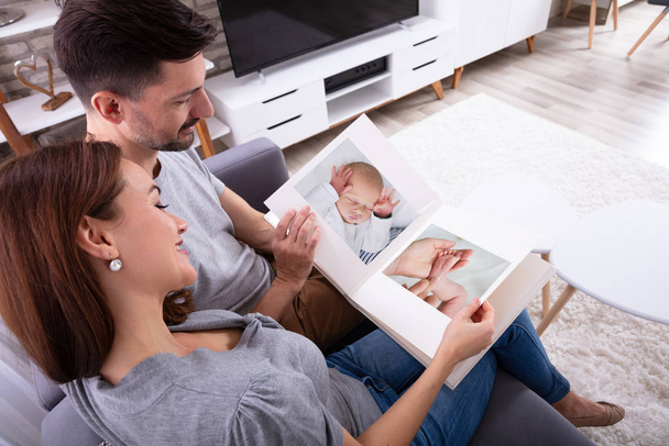 Close-up Of Couple Looking At Baby's Photo Album In - Foto, Imagen