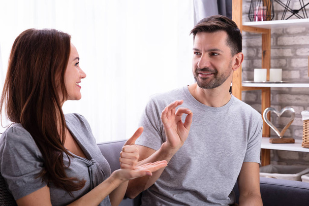 Smiling Young Couple Sitting On Sofa Communicating With Sign Languages - Photo, Image