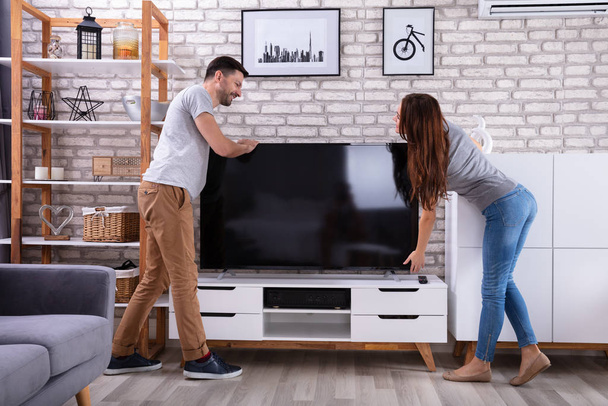 Side View Of Young Couple Lifting Television At Home - Foto, imagen