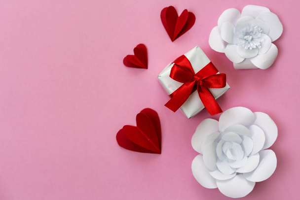 Romantic present in a box with red ribbon, 3d red hearts and white flowers, copy space on left side. - Photo, Image