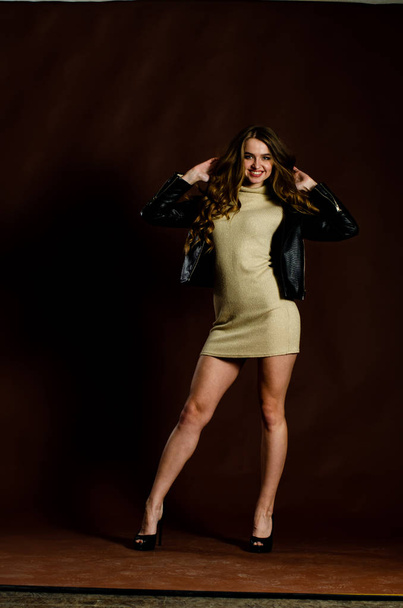 sensual attractive woman in shiny dress with leather jacket and high heels posing on black background  - Foto, Imagen
