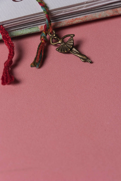 Primer plano de separadores de cuaderno hechos a mano con hilo trenzado con bailarina en cobre en la punta, sobre una mesa rosada - Foto, Imagem