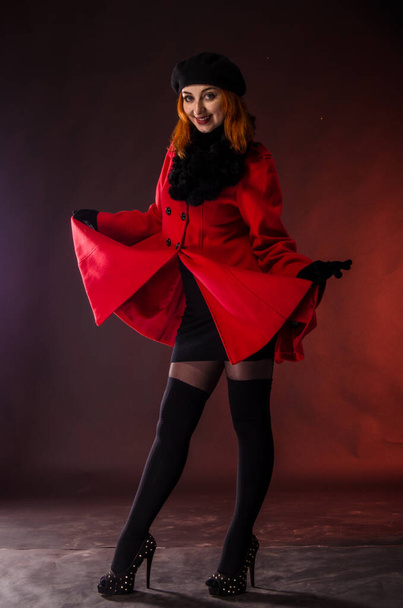 Fashion model in red coat looking down with smile on her face - Zdjęcie, obraz