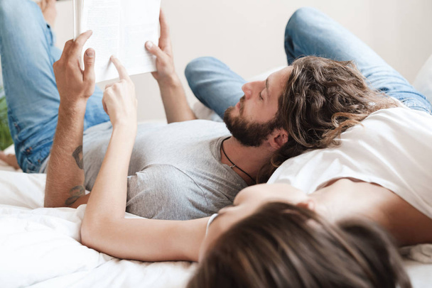 Loving couple indoors at home lies reading book together. - 写真・画像