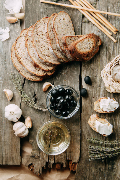 Sliced bread and garlic on a wooden background. Olives in a bowl of oil. Flatley's Italian food.  - Foto, imagen
