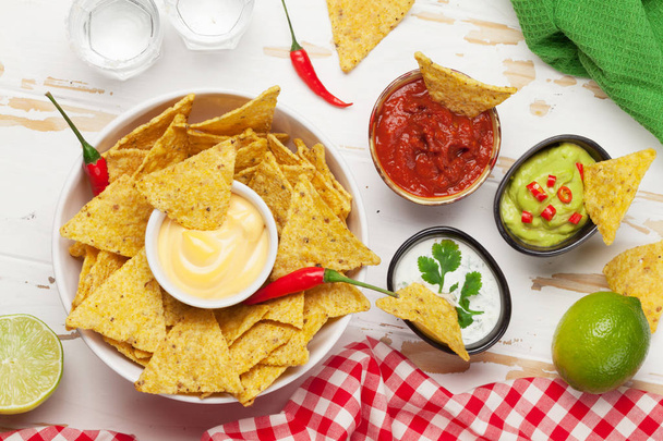 mexikanische Nachos-Chips mit verschiedenen Soßen - Guacamole, Salsa, Käse und saure Sahne. Draufsicht flach auf Holztisch mit zwei Tequila-Shots - Foto, Bild