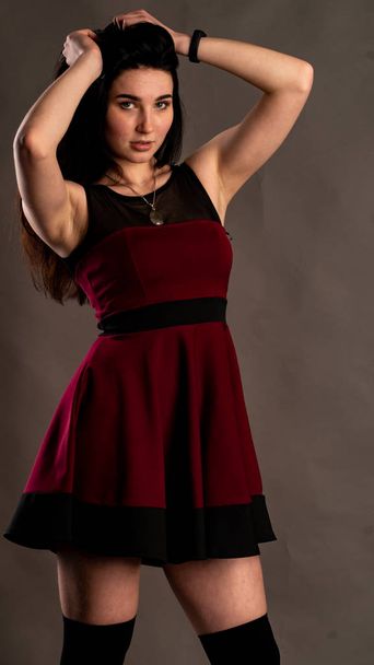 Bonito modelo sexy joven hembra con pelo oscuro y vestido rojo, posando en estudio oscuro.. - Foto, Imagen
