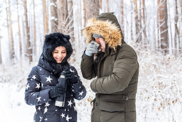 Young couple in love drink a hot drink from a thermos and enjoy winter nature. - Photo, Image