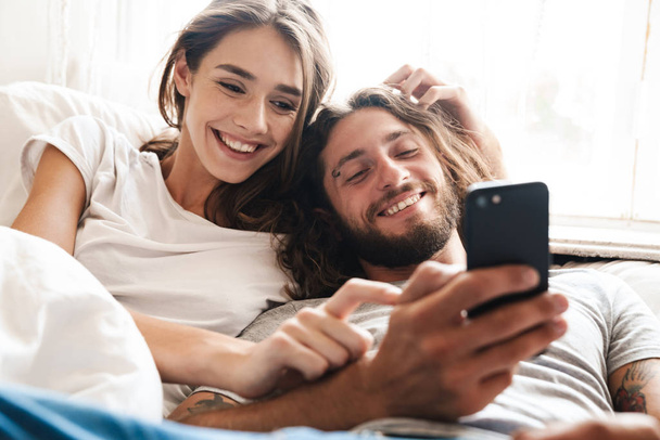 Loving couple indoors at home lies using mobile phone together. - Foto, immagini