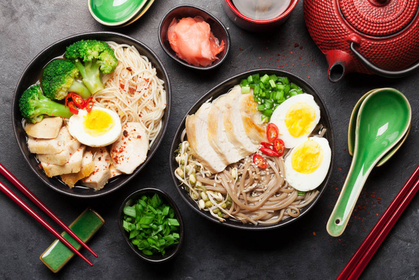 Aziatische noedelsoep met kip, groenten en eieren en kruidenthee op stenen ondergrond. Bovenaanzicht vlak lay - Foto, afbeelding