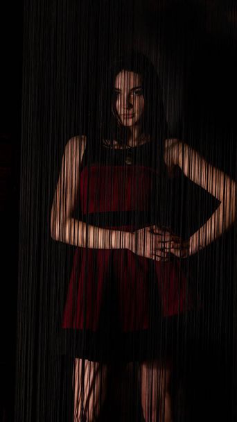 Grazioso giovane modello sexy femmina con i capelli scuri in abito rosso posa in studio scuro. - Foto, immagini