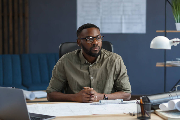 Afro-American architect working in office with laptop.Business portrait of black handsome bearded man wearing eyeglasses sitting at workplace.Confident businessman became successful.Business concept - Foto, immagini