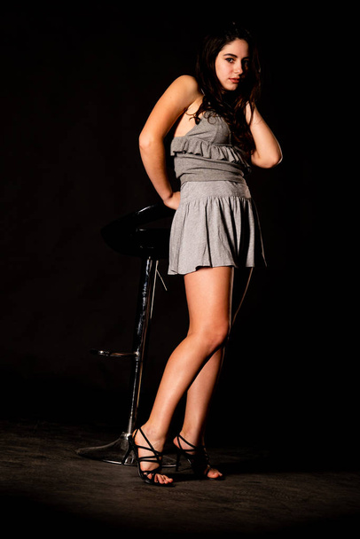 piękna kobieta z ciemnymi brunetkami włosy w szare ubrania pozowanie na ciemnym tle studio   - Zdjęcie, obraz
