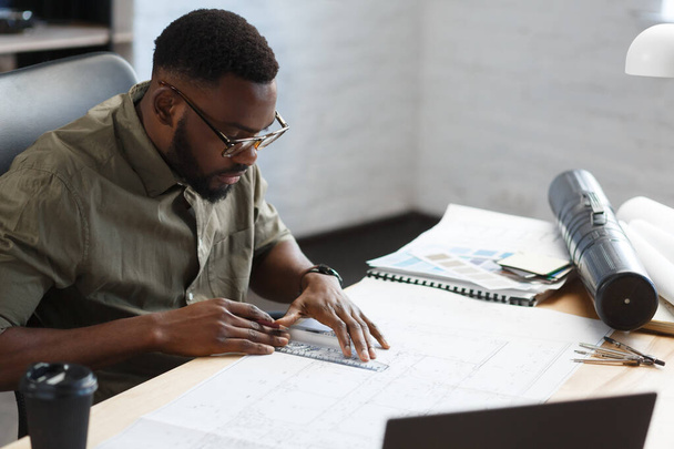 Afro-American architect working in office with blueprints.Engineer inspect architectural plan, sketching a construction project. Portrait of black handsome man sitting at workplace. Business concept - Foto, Bild