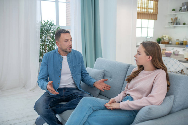 Dad talking to sad daughter, both sitting on the couch. - Photo, Image
