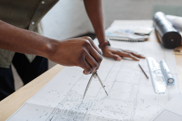 Afro-Amerikaanse architect werkt in het kantoor met blauwdrukken. Ingenieur inspecteren architectonisch plan, schetsen van een bouwproject. Portret van een zwarte knappe man op het werk. Bedrijfsconcept - Foto, afbeelding