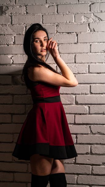 Muito jovem modelo sexy feminino com cabelos escuros em vestido vermelho posando em estúdio escuro. - Foto, Imagem