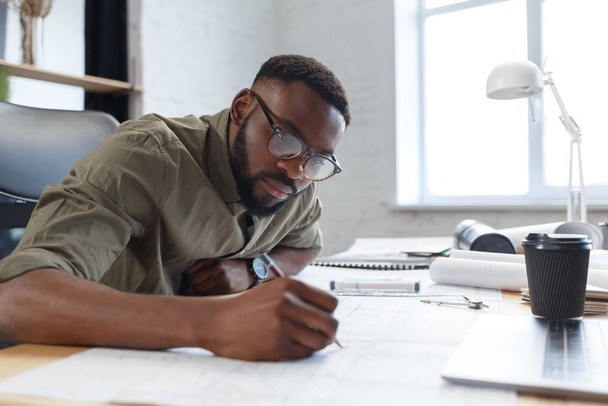 Afro-American architect working in office with blueprints.Engineer inspect architectural plan, sketching a construction project. Portrait of black handsome man sitting at workplace. Business concept - Фото, зображення