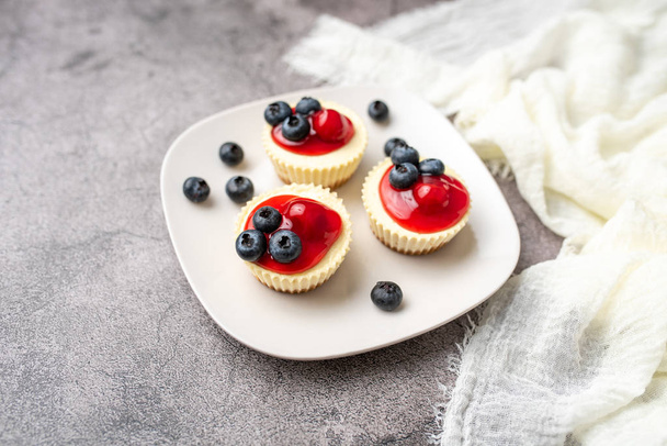 Mini cheesecakes with cherry and blueberry topping, sweet summer treat - Foto, afbeelding