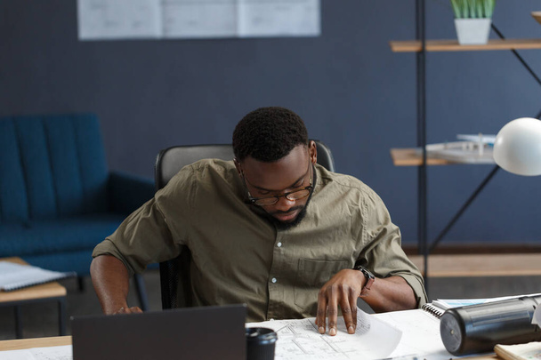 Afro-American architect working in office with blueprints.Engineer inspect architectural plan, sketching a construction project. Portrait of black handsome man sitting at workplace. Business concept - Foto, immagini