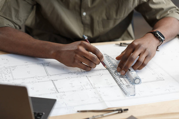 Afro-Amerikaanse architect werkt in het kantoor met blauwdrukken. Ingenieur inspecteren architectonisch plan, schetsen van een bouwproject. Portret van een zwarte knappe man op het werk. Bedrijfsconcept - Foto, afbeelding