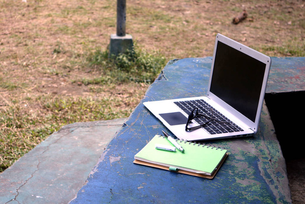 aptop υπολογιστή, γυαλιά ηλίου, σημειωματάριο και στυλό σε υπαίθριο πάρκο - Φωτογραφία, εικόνα