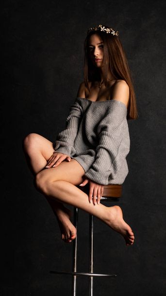 Sexy jovem em belo vestido cinza com mangas posando no estúdio na cadeira Em um fundo preto  - Foto, Imagem