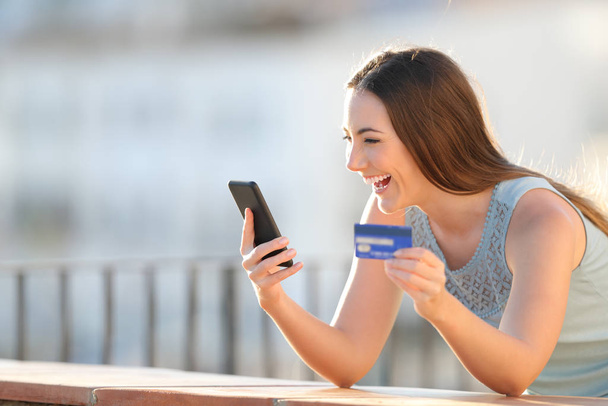 Excited girl is paying with credit card and smart phone in a balcony - 写真・画像