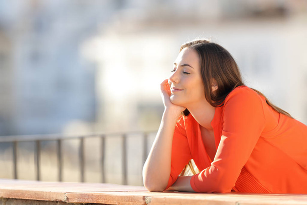 Happy woman in orange relaxing and meditating in a balcony - Photo, image