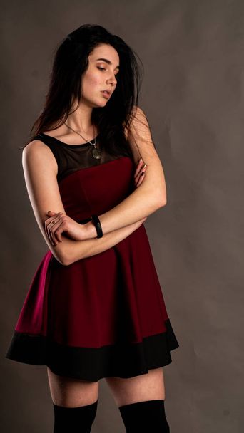 Pretty young sexy model female with dark hair in red dress posing in dark studio. - Фото, зображення