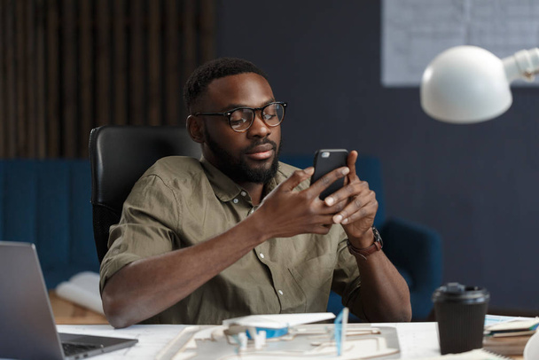 Young Afro-American man using smartphone and smiling. Happy businessman using mobile phone apps, texting message, browsing internet, looking at smartphone. Young people working with mobile devices - Valokuva, kuva
