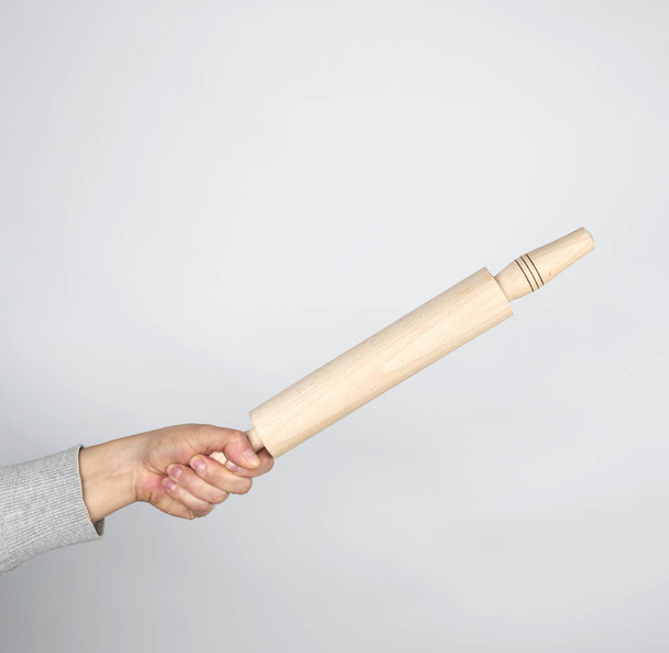 mão segurando um rolo de madeira em um fundo cinza
 - Foto, Imagem
