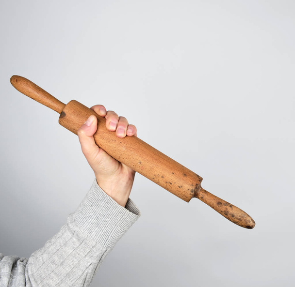hand holding old wooden rolling pin on a gray background - Foto, Imagen