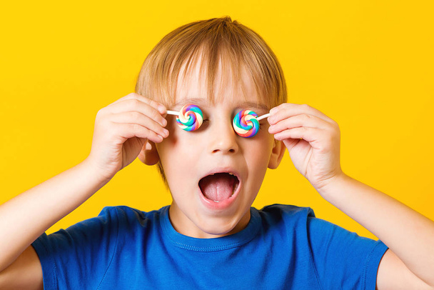 A criança cobriu olhos de lolipops. Bonito menino animado sobre fundo amarelo
 - Foto, Imagem