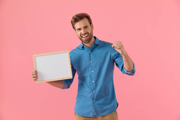 happy casual guy holding empty board and celebrating victory - Photo, Image