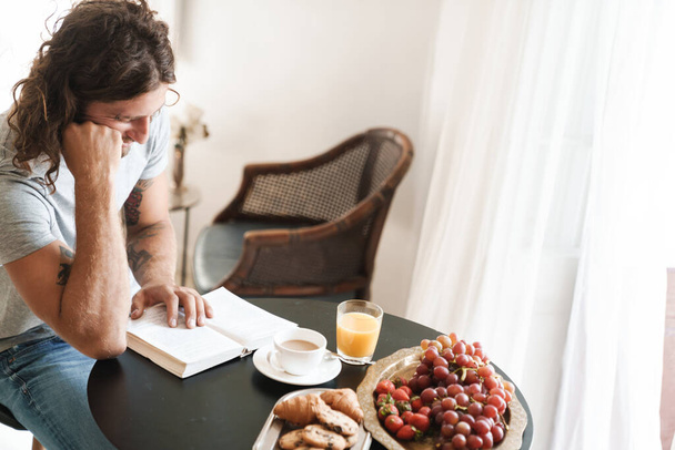 Man sit at the table indoors at home have a breakfast reading book. - Foto, immagini