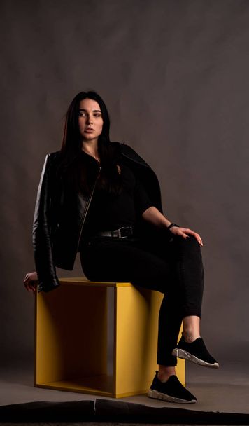 mladá brunetka žena ve stylovém oblečení pózuje v tmavém studiu   - Fotografie, Obrázek