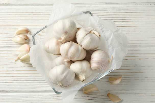 Glass bowl of fresh garlic bulbs, slices on white wooden backgro - Foto, afbeelding