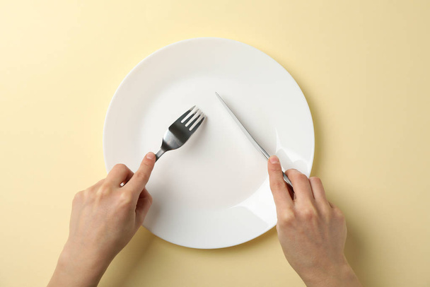 Female hands hold fork and knife on beige background with plate, - Photo, image