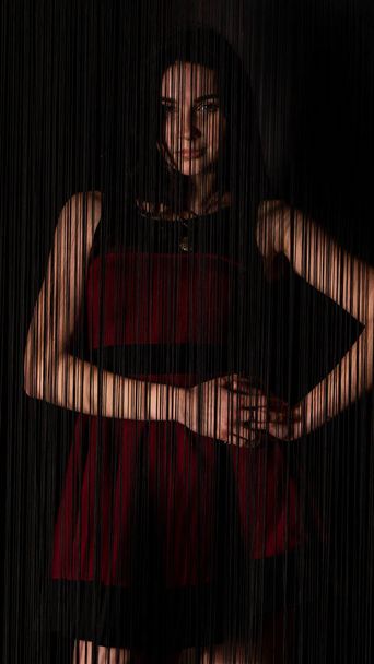 vrij jong sexy model vrouw met donker haar in rood jurk poseren in donker studio. - Foto, afbeelding