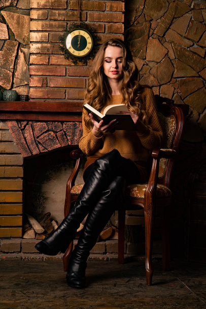 atraente jovem mulher sentado na cadeira perto de lareira em estúdio   - Foto, Imagem